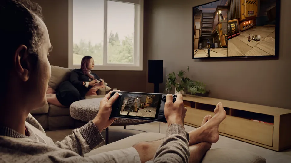 Player on a living room couch holding a Steam Deck, with a game shown on a wall-mounted TV