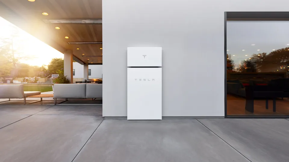 Two white Tesla Powerwall units mounted on the outside wall of a modern house at sunset