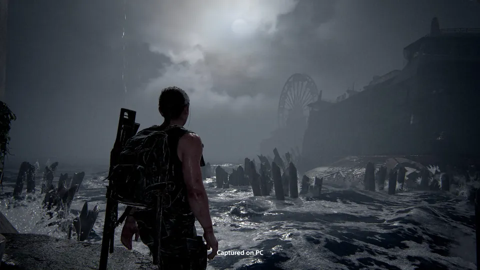 A survivor standing on a stormy shore near a Ferris wheel in The Last of Us Part II Remastered