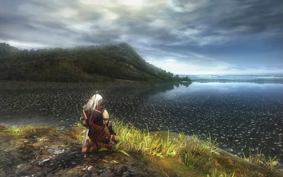 Geralt kneels on a lakeshore under a cloudy sky in the original Witcher