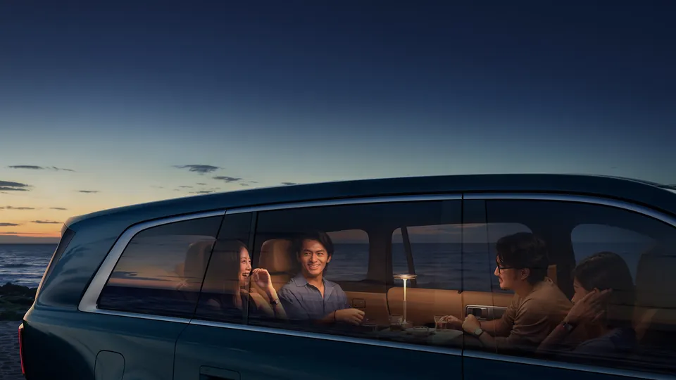 Four passengers sitting face to face inside a Xiaomi Pengcheng N90 Max at dusk, seen through the side windows