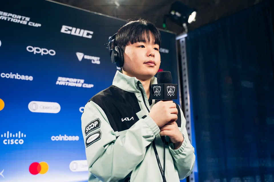 A Dplus KIA player in a mint team jacket holds a Worlds microphone at the Worlds 2026 Swiss Stage media day