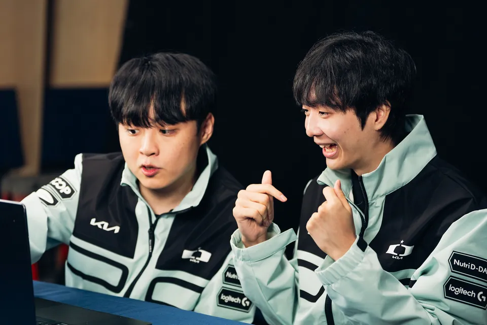 Two Dplus KIA players in mint team jackets laugh at a desk at the Worlds 2026 Swiss Stage media day