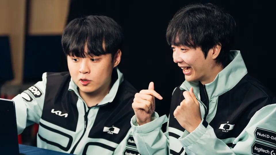 Two Dplus KIA players in mint team jackets laugh at a desk at the Worlds 2026 Swiss Stage media day