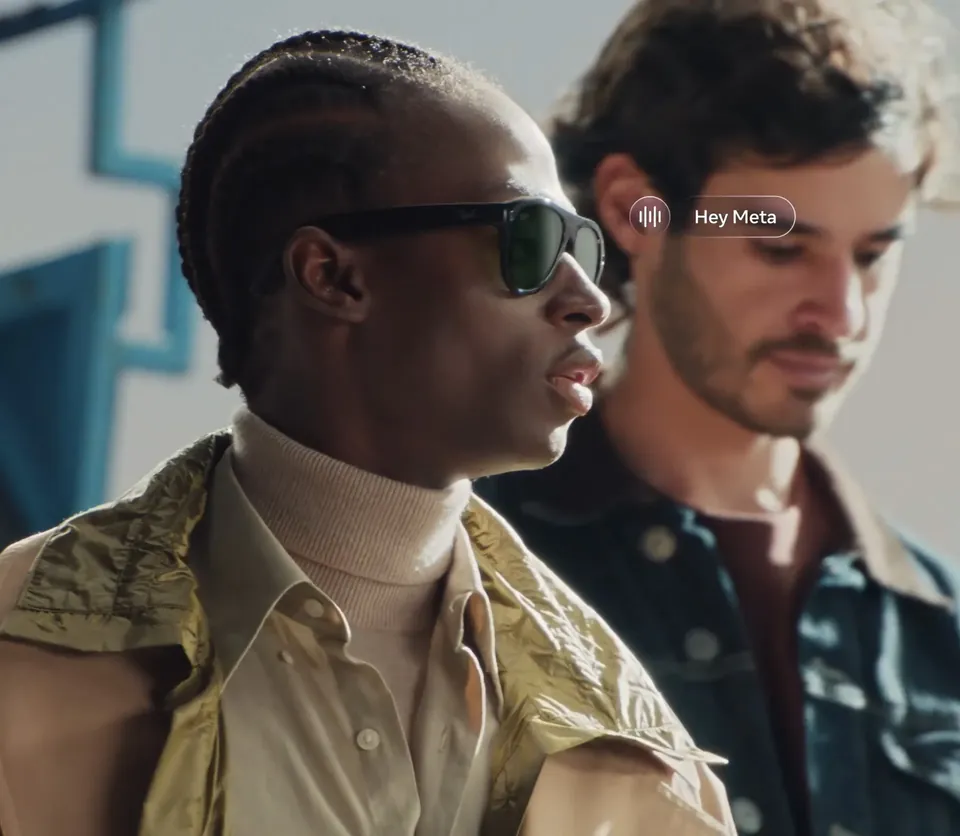 A man in dark Ray-Ban Meta sunglasses talks to the glasses assistant, with a Hey Meta prompt on screen