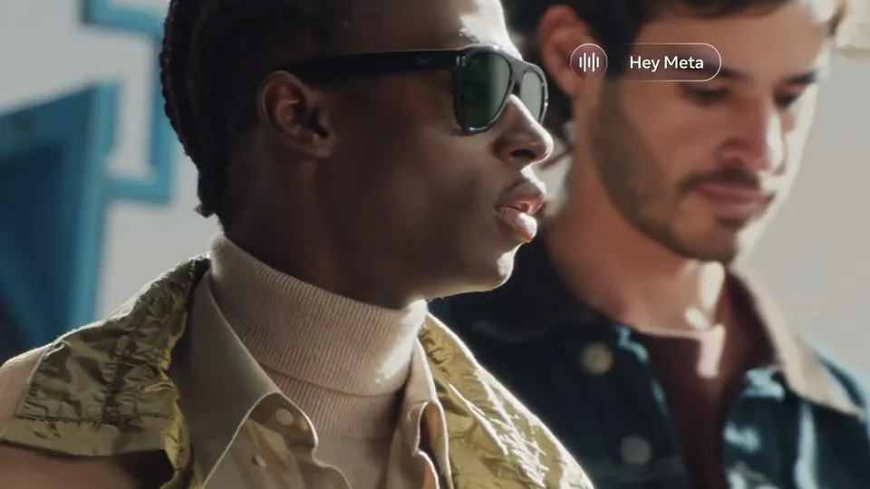 A man in dark Ray-Ban Meta sunglasses talks to the glasses assistant, with a Hey Meta prompt on screen