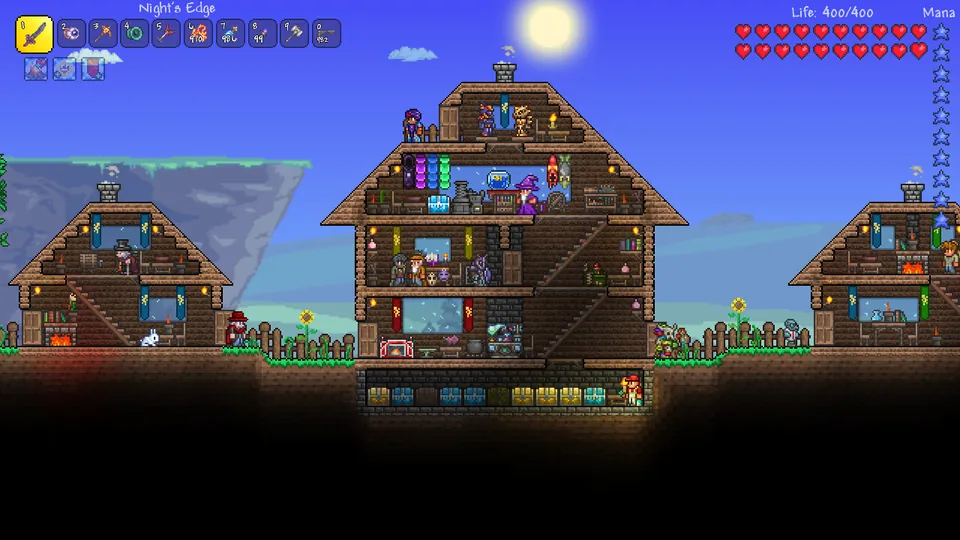A small village of wooden houses filled with furniture and townspeople stands on a grassy hill under the sun in Terraria