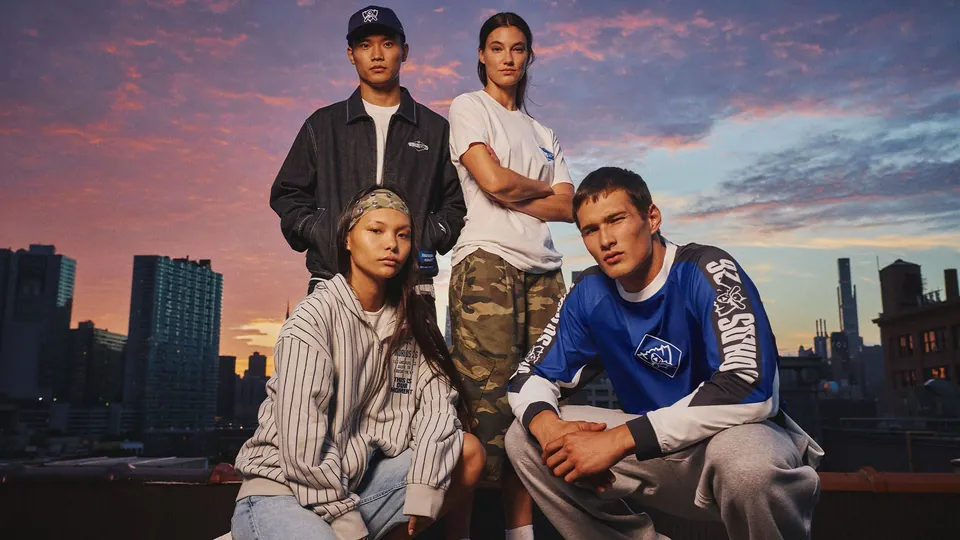 Four models in Riot's Worlds 2026 collection on a New York rooftop at sunset, one in a blue Worlds shirt