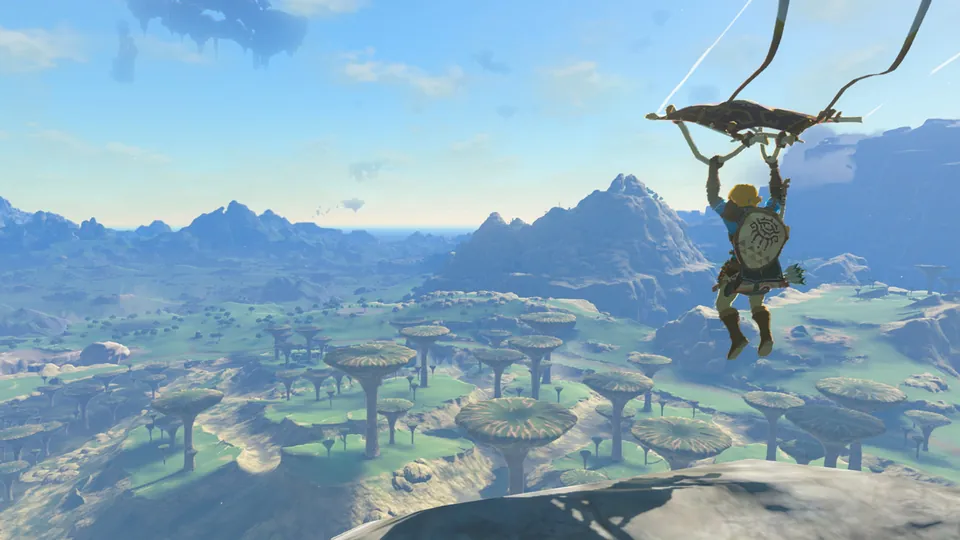 Link glides on a paraglider over a wide green valley dotted with rock formations in The Legend of Zelda: Tears of the Kingdom