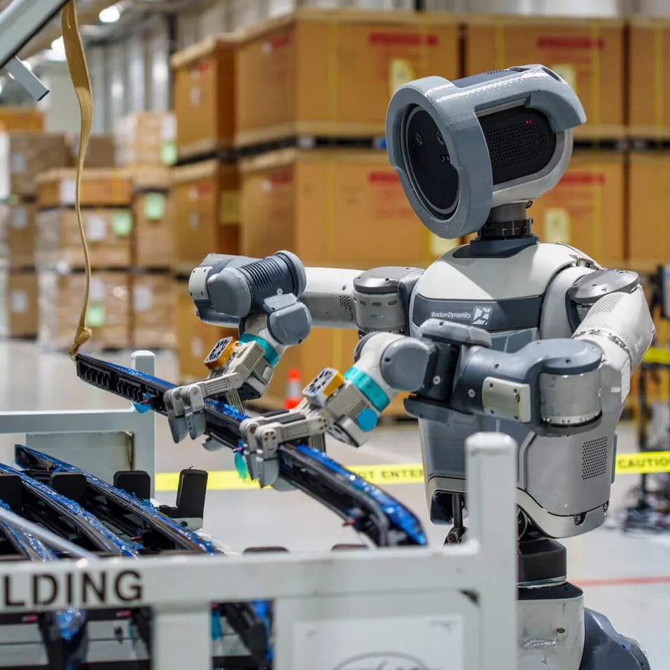 Atlas holds a part at a factory cart with shelves of boxes behind it