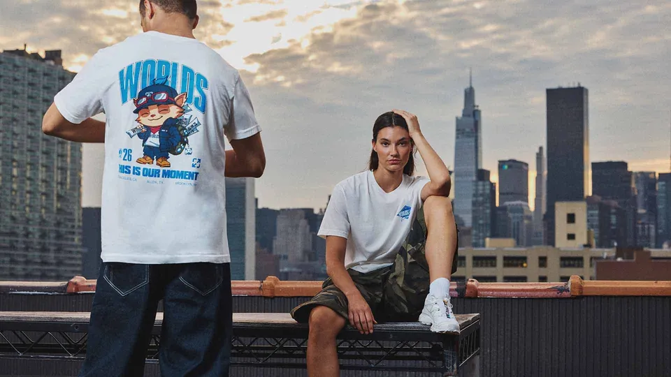 Two people in Worlds 2026 T-shirts on a rooftop, one standing and one seated, with the New York City skyline behind them