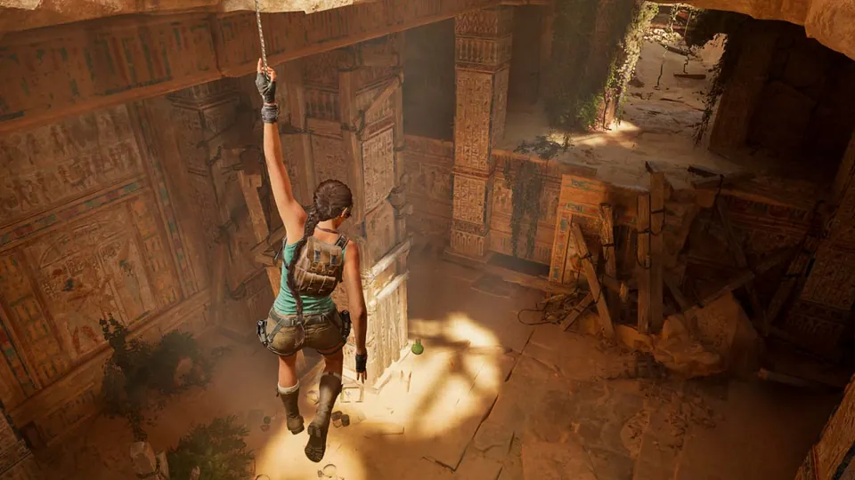 Lara Croft climbs down a rope into a sunlit Egyptian tomb covered in hieroglyphs in Tomb Raider: Legacy of Atlantis