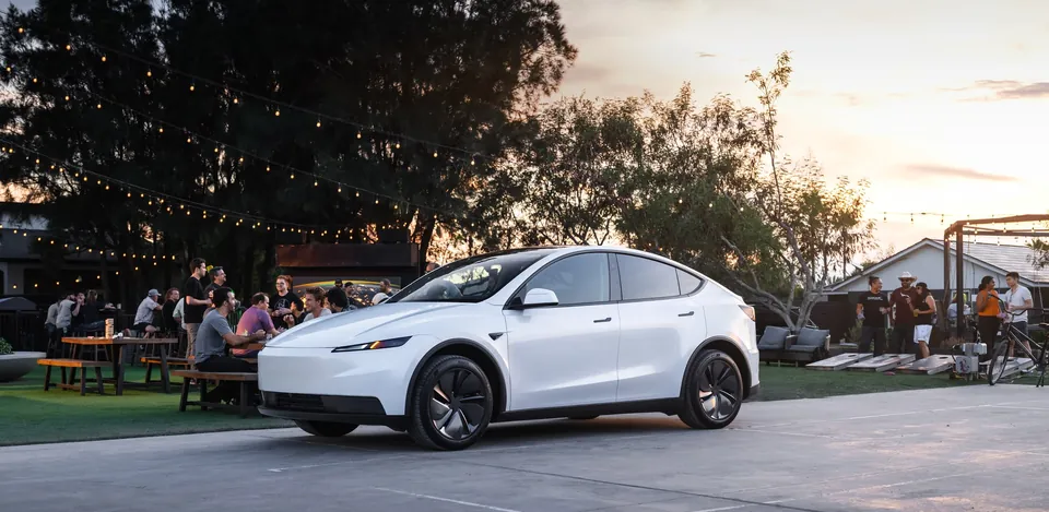 A white Tesla Model Y parked beside an outdoor gathering at sunset