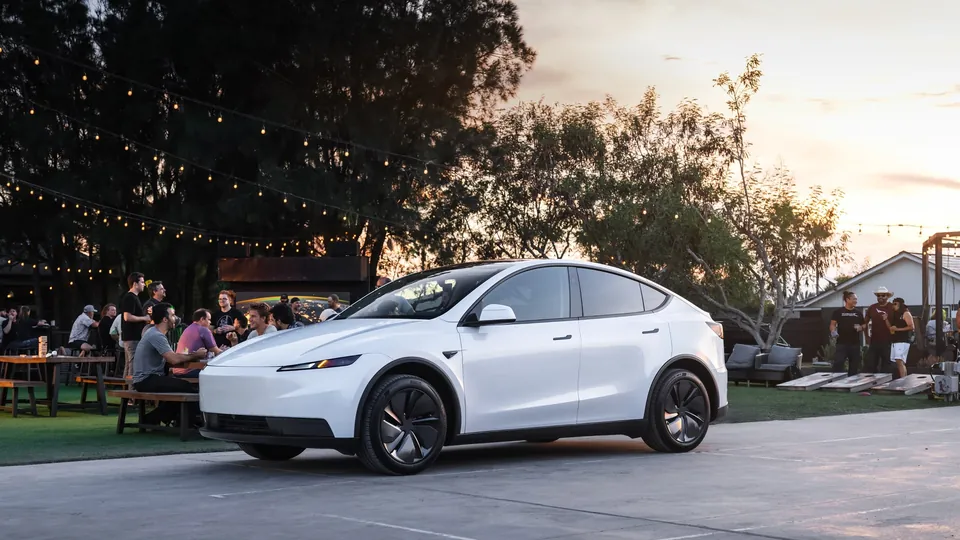 A white Tesla Model Y parked beside an outdoor gathering at sunset