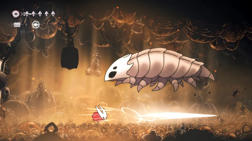 Hornet dashes under a huge pale grub in a golden cavern in Hollow Knight: Silksong