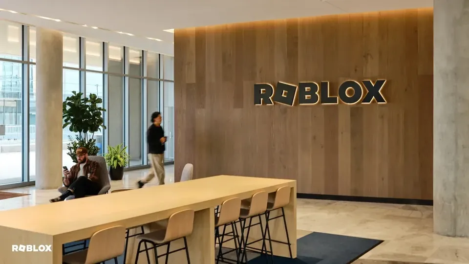 The Roblox logo on a wooden wall in the lobby of a Roblox office, with long tables and chairs in front