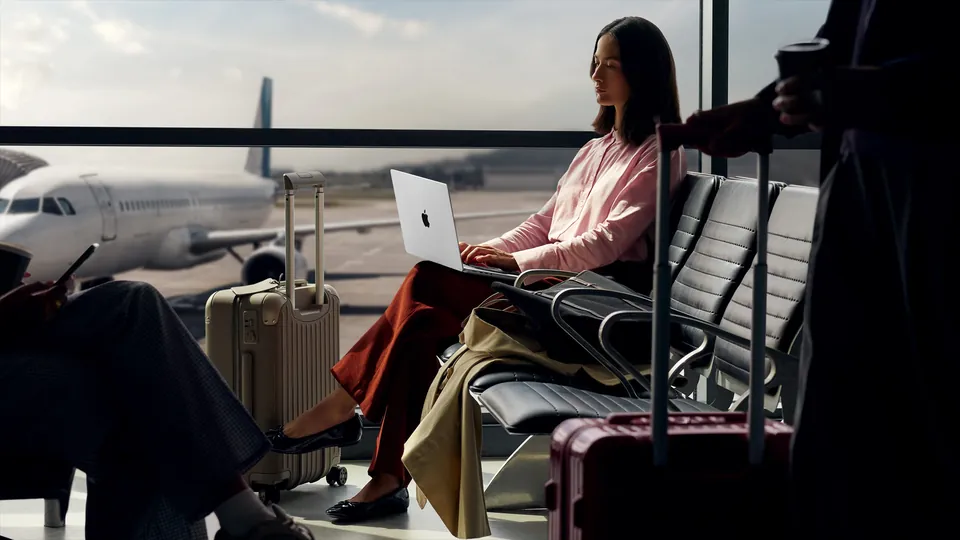 A traveler works on a silver MacBook Pro in an airport lounge