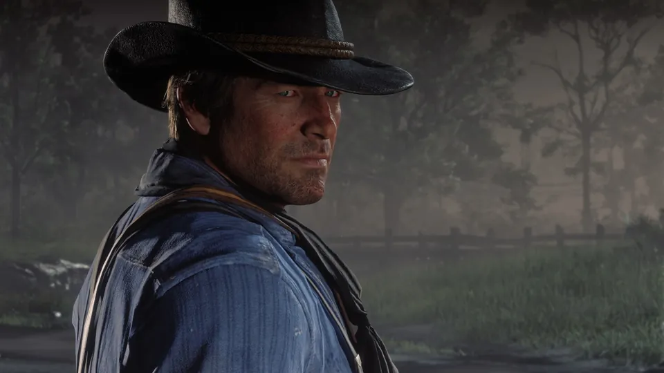 Arthur Morgan, in a black hat and blue shirt, glances back in a misty field in Red Dead Redemption 2