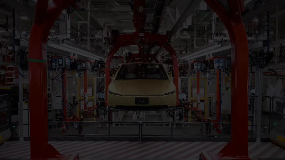 A gold Tesla Cybercab on a Tesla production line, framed by red assembly-line arches